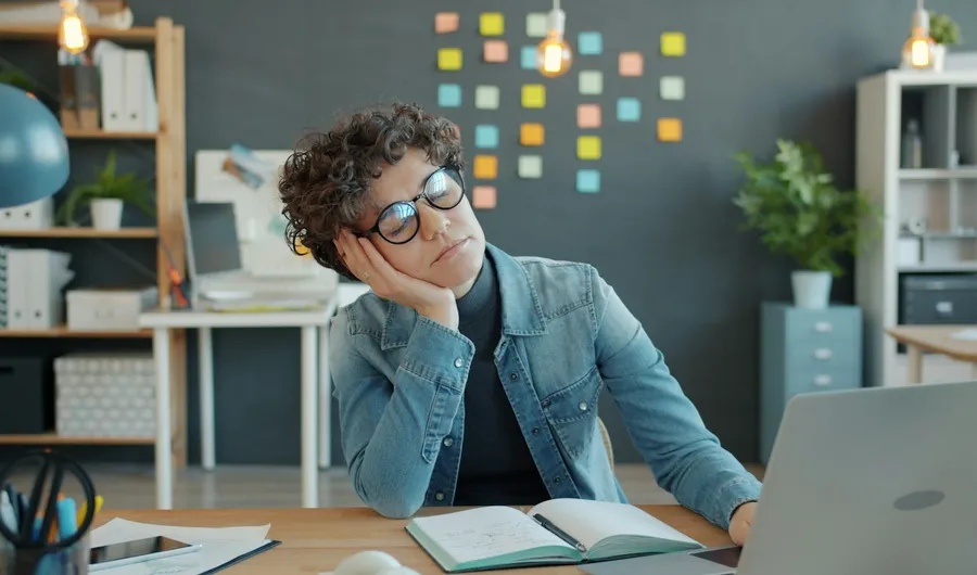 A tired woman resting her head on her hand at her desk