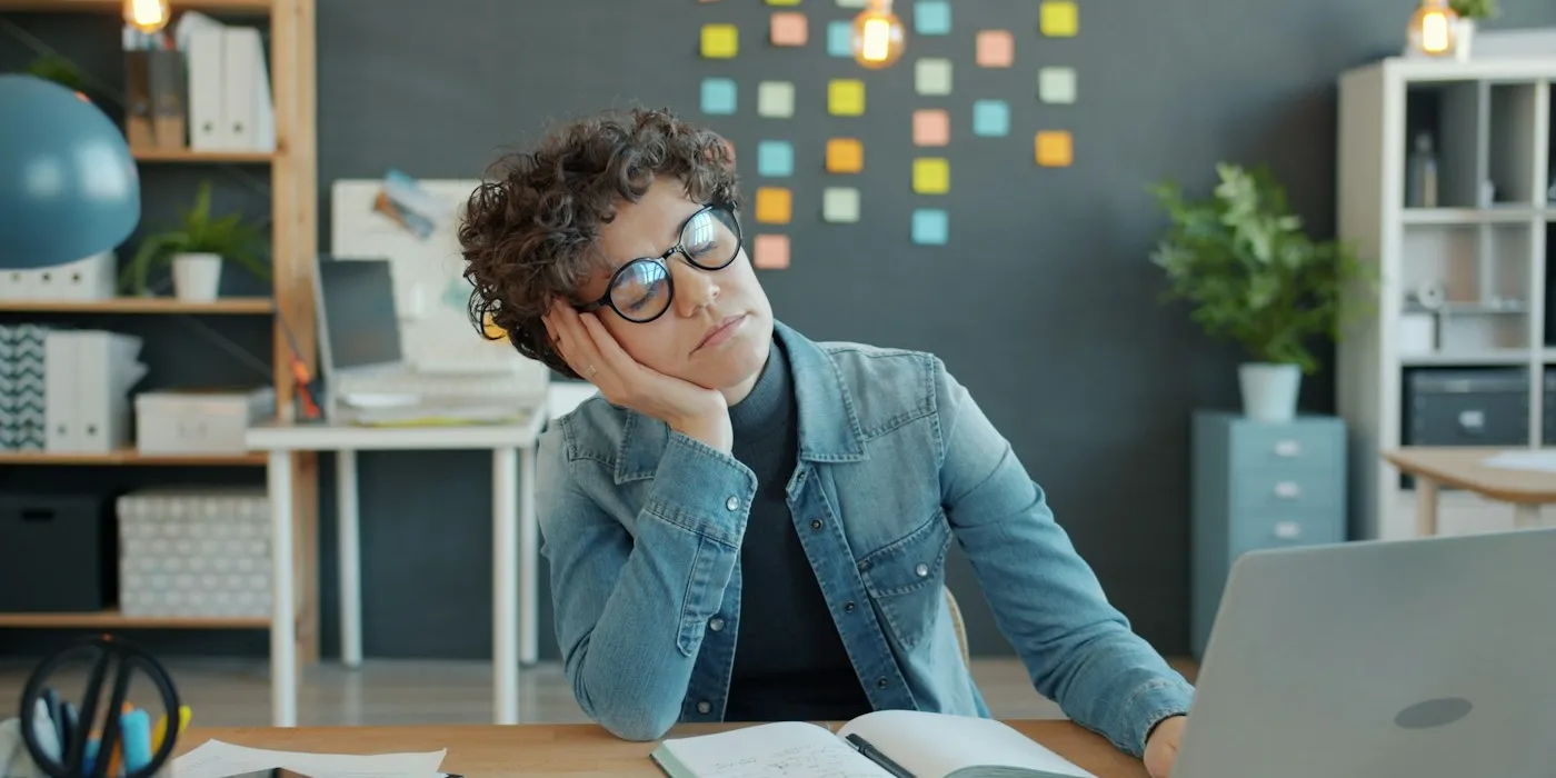 A tired woman resting her head on her hand at her desk